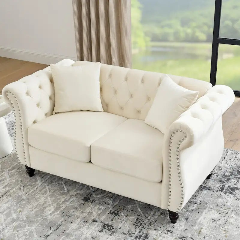 Canapé Chesterfield deux places en velours beige, accoudoirs arrondis, garniture cloutée